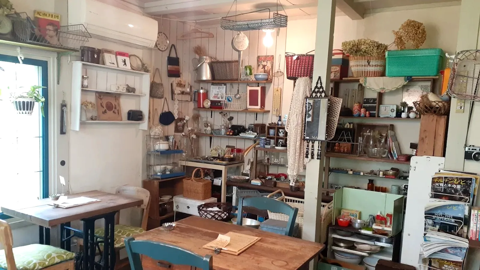 cafe & curio snoozeの店内。青枠の窓から光が入り、木のテーブルとティールの椅子、古道具の並ぶ棚が見える