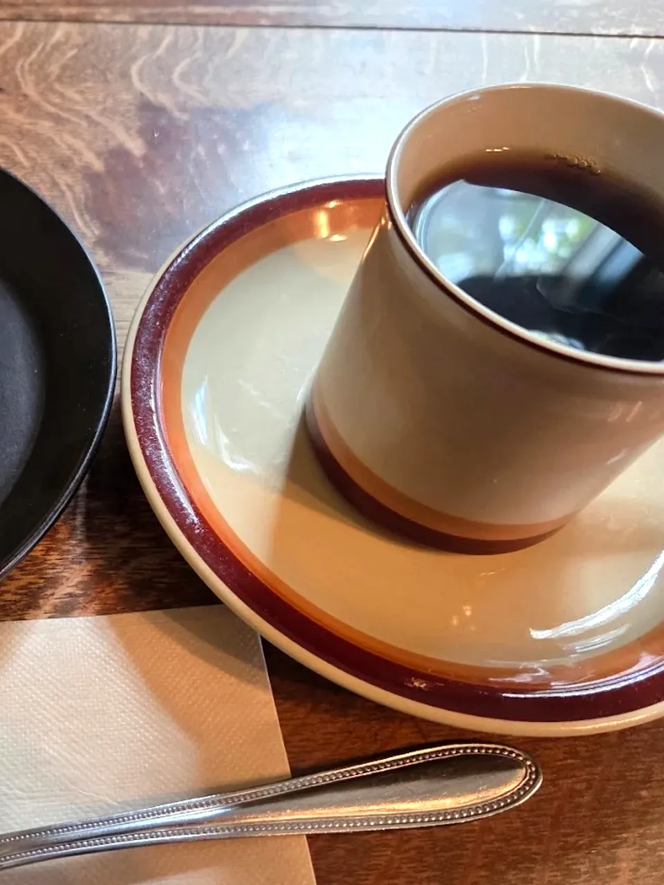 黒い皿にのったチーズケーキと、レトロなブラウンリムのカップのコーヒー