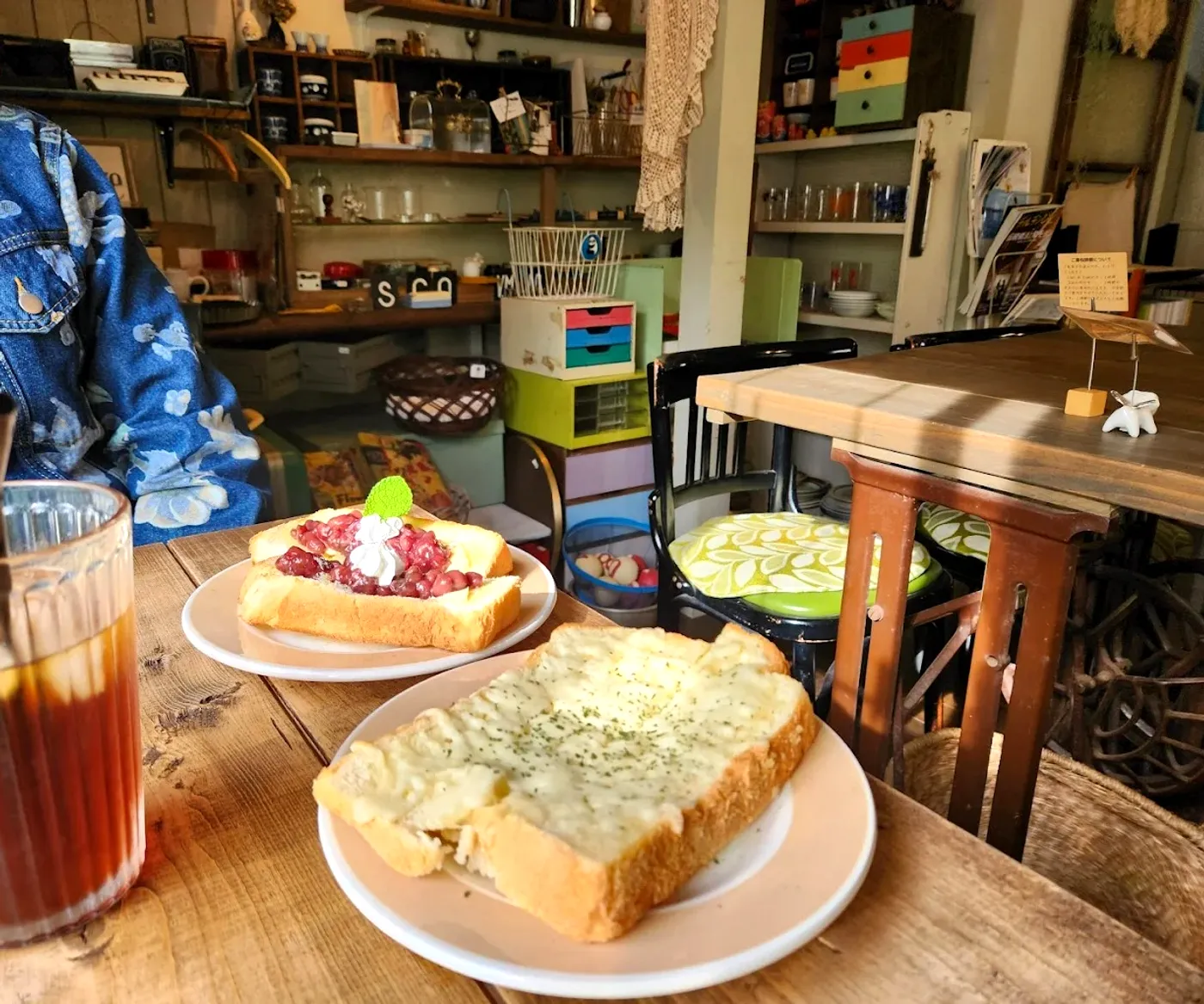 手前にトーストの皿とアイスドリンク、奥に古道具の棚とミシン脚のテーブルが並ぶ店内